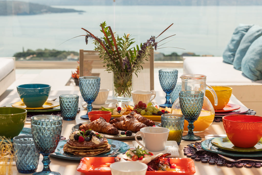 Dining table set with colorful tableware and food, overlooking a scenic view.