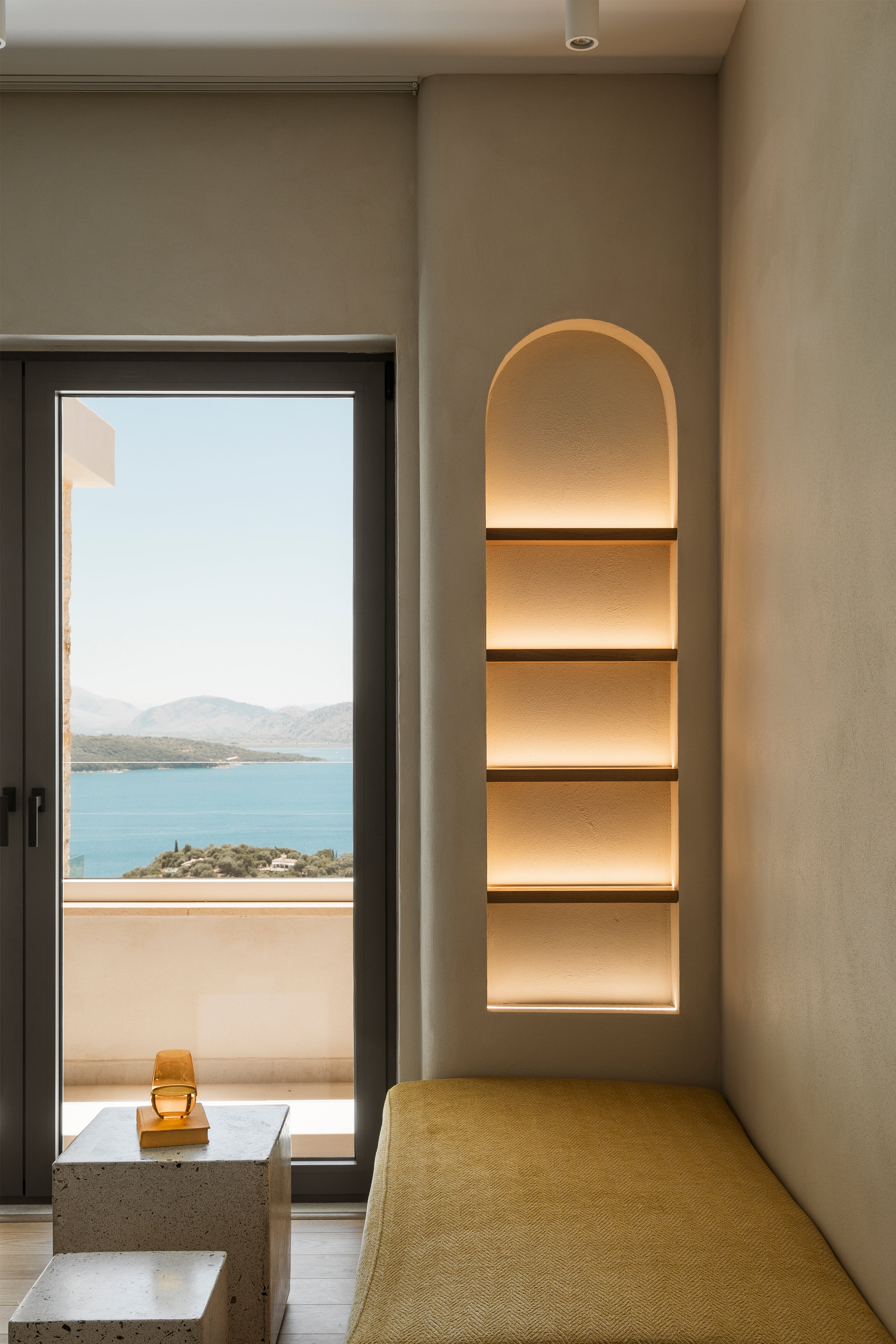 Modern interior with a shelf, bench, and view of water and mountains.
