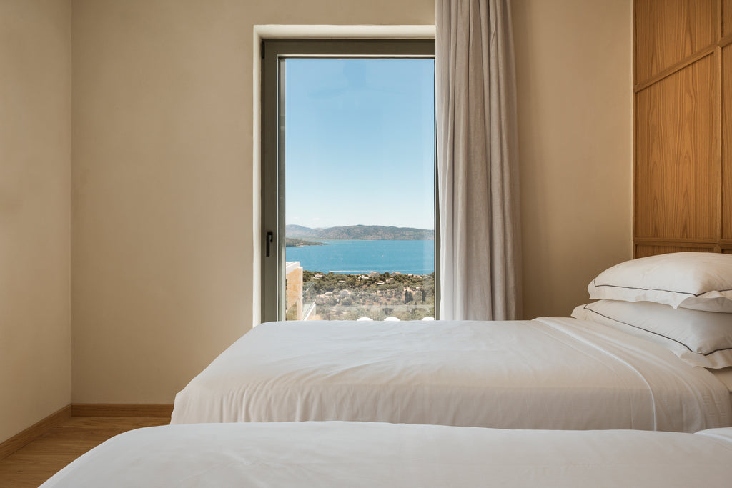 Bedroom with two beds and a large window overlooking a scenic view of water and mountains.
