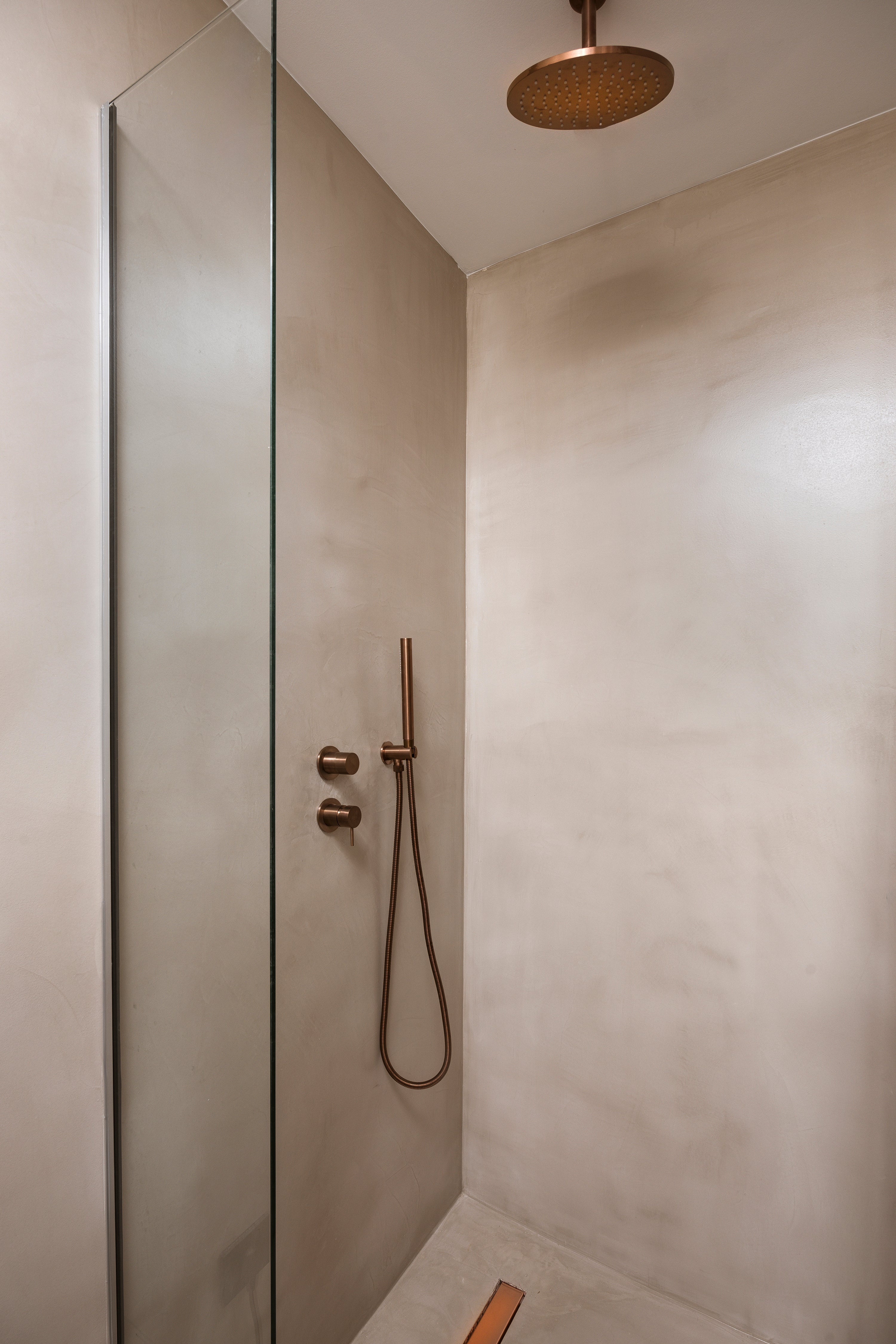 Modern shower setup with glass door and metallic fixtures in a neutral-toned bathroom.