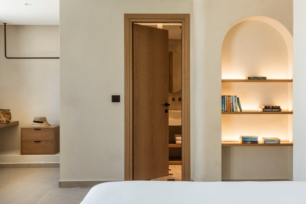 Modern bedroom with open door leading to bathroom, shelves with books and decor.