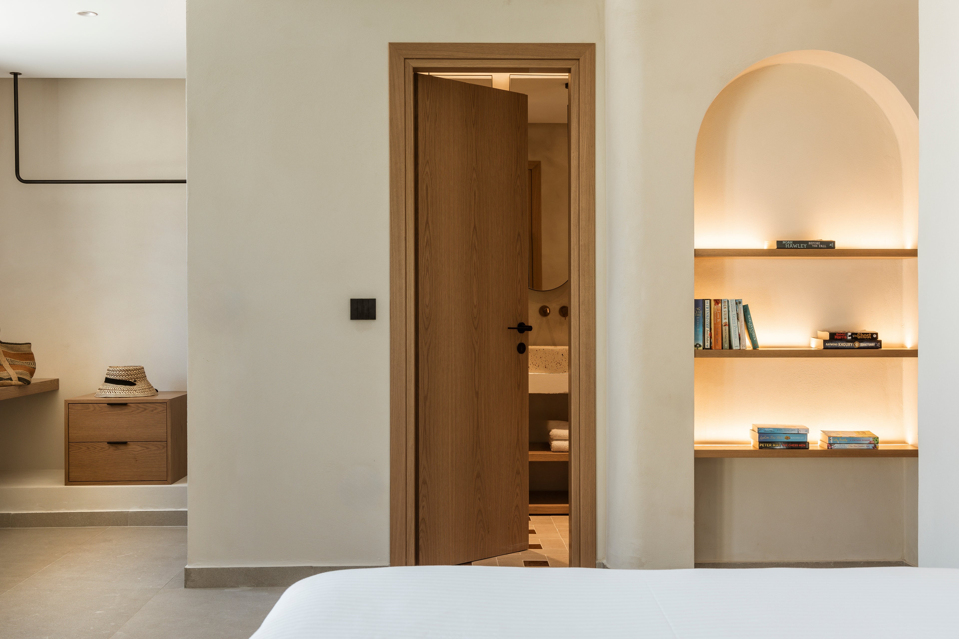 Modern bedroom with open door leading to bathroom, shelves with books and decor.