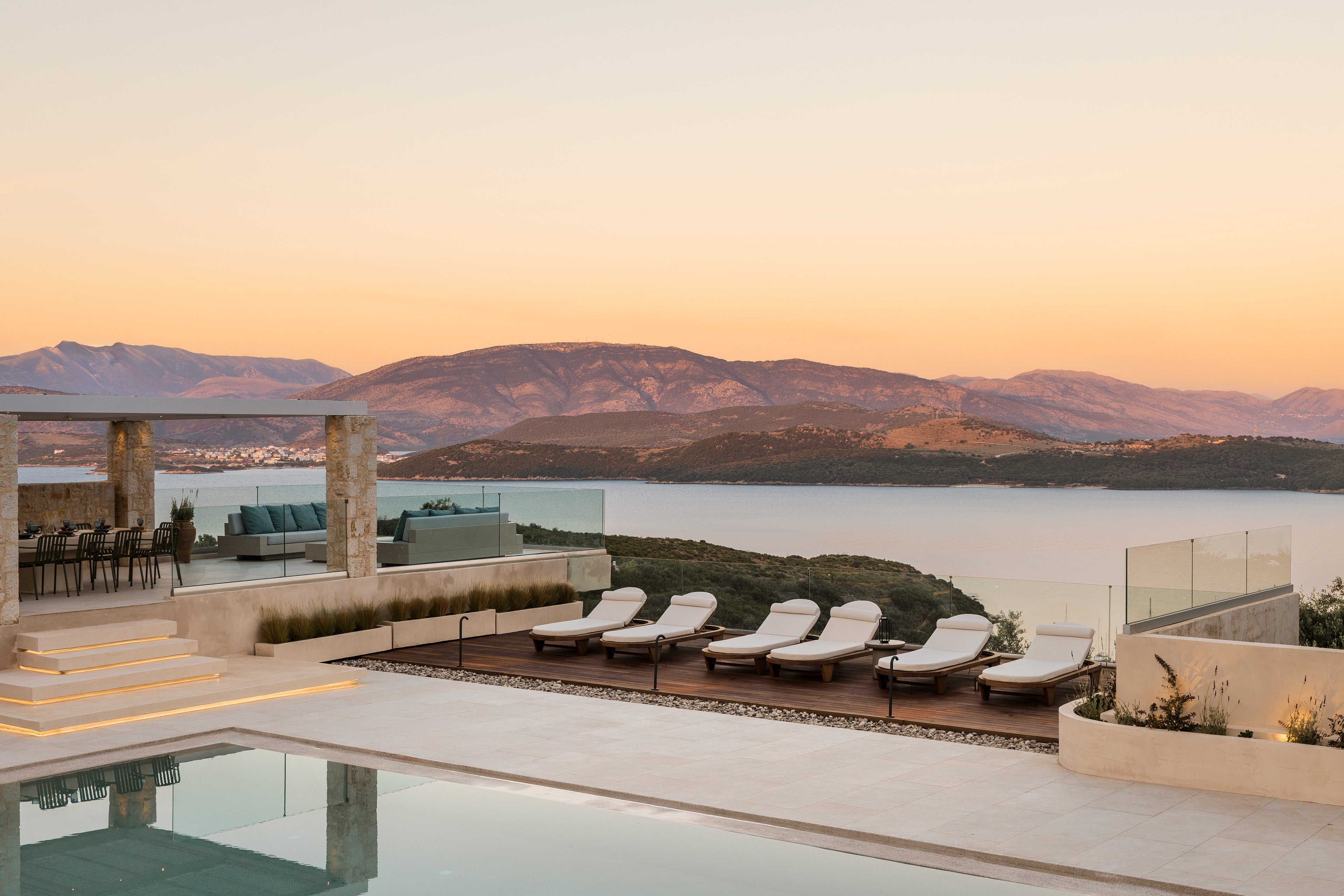 Outdoor pool area with lounge chairs and a scenic view of mountains and water.