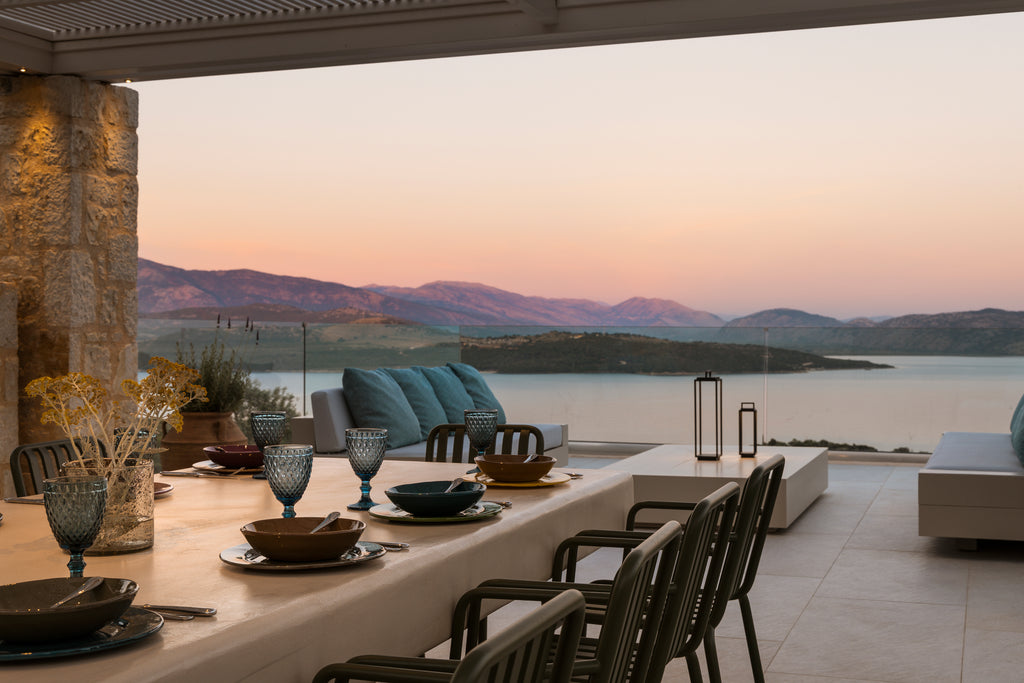 Outdoor dining area with scenic view of mountains and water at sunset.