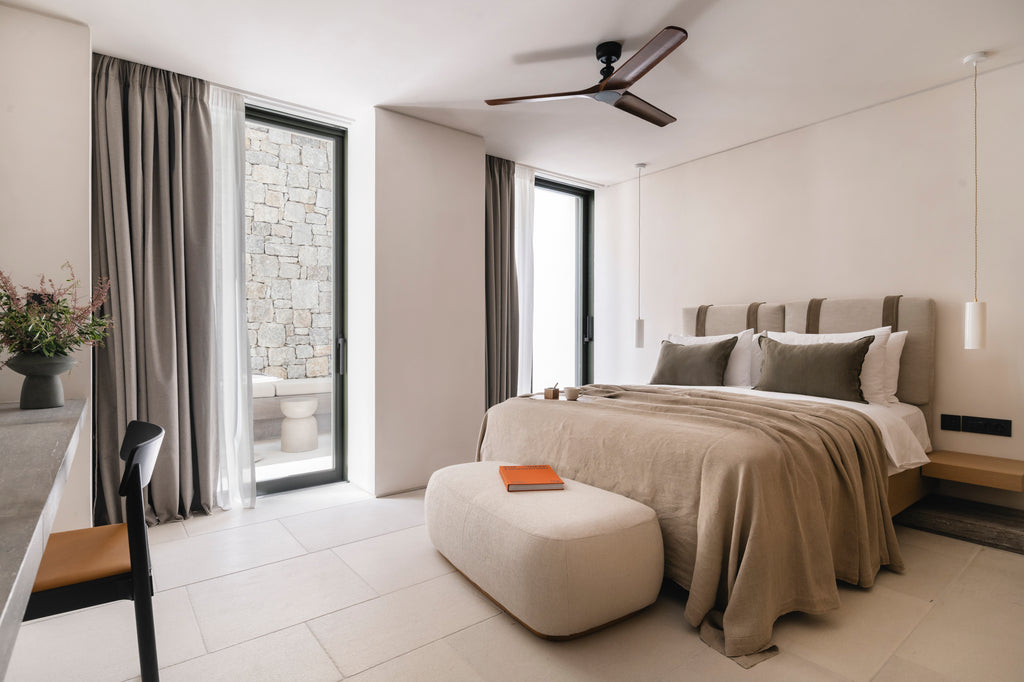 Modern bedroom with a bed, ottoman, and large windows.