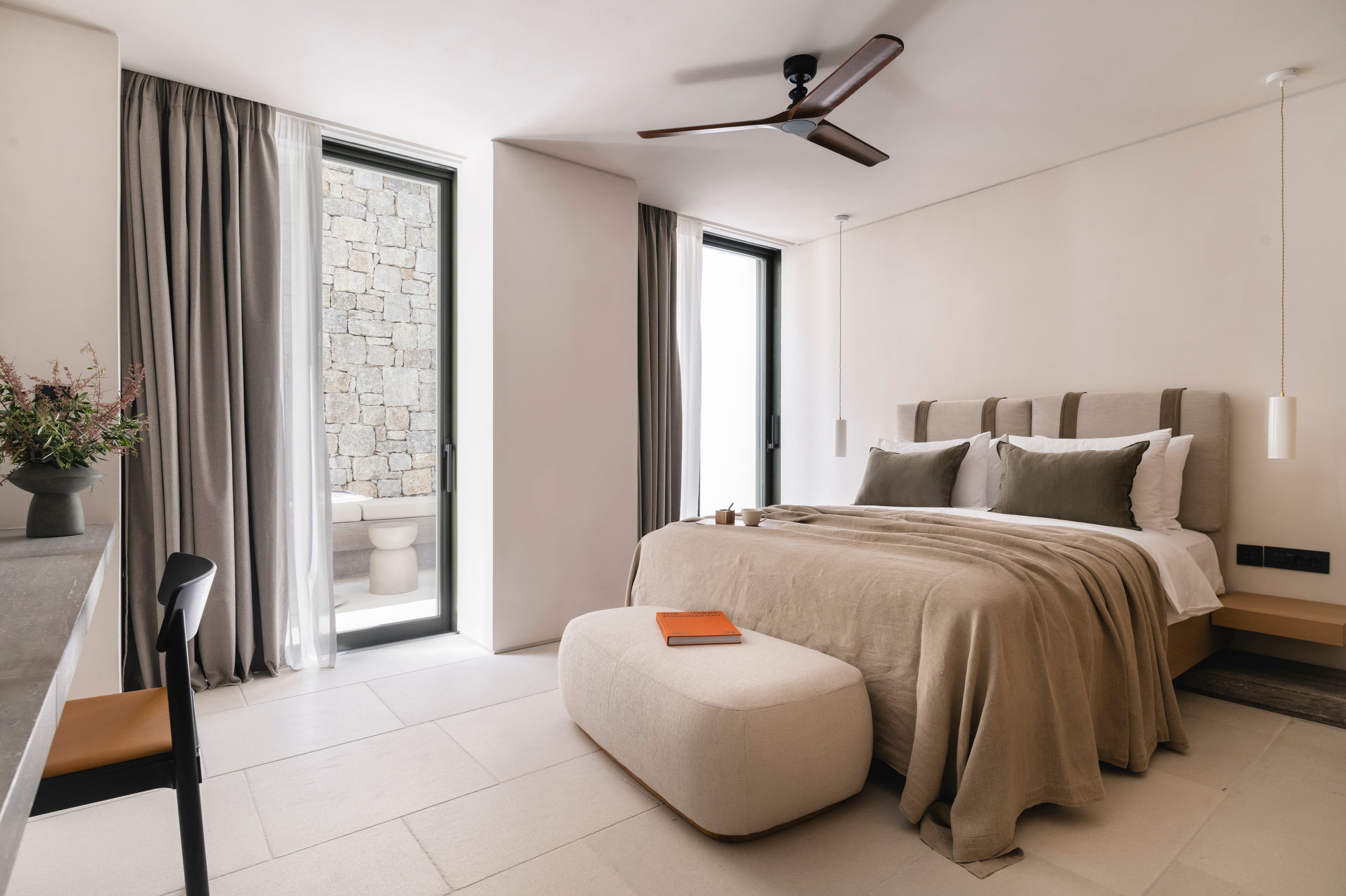 Modern bedroom with a bed, ottoman, and large windows.