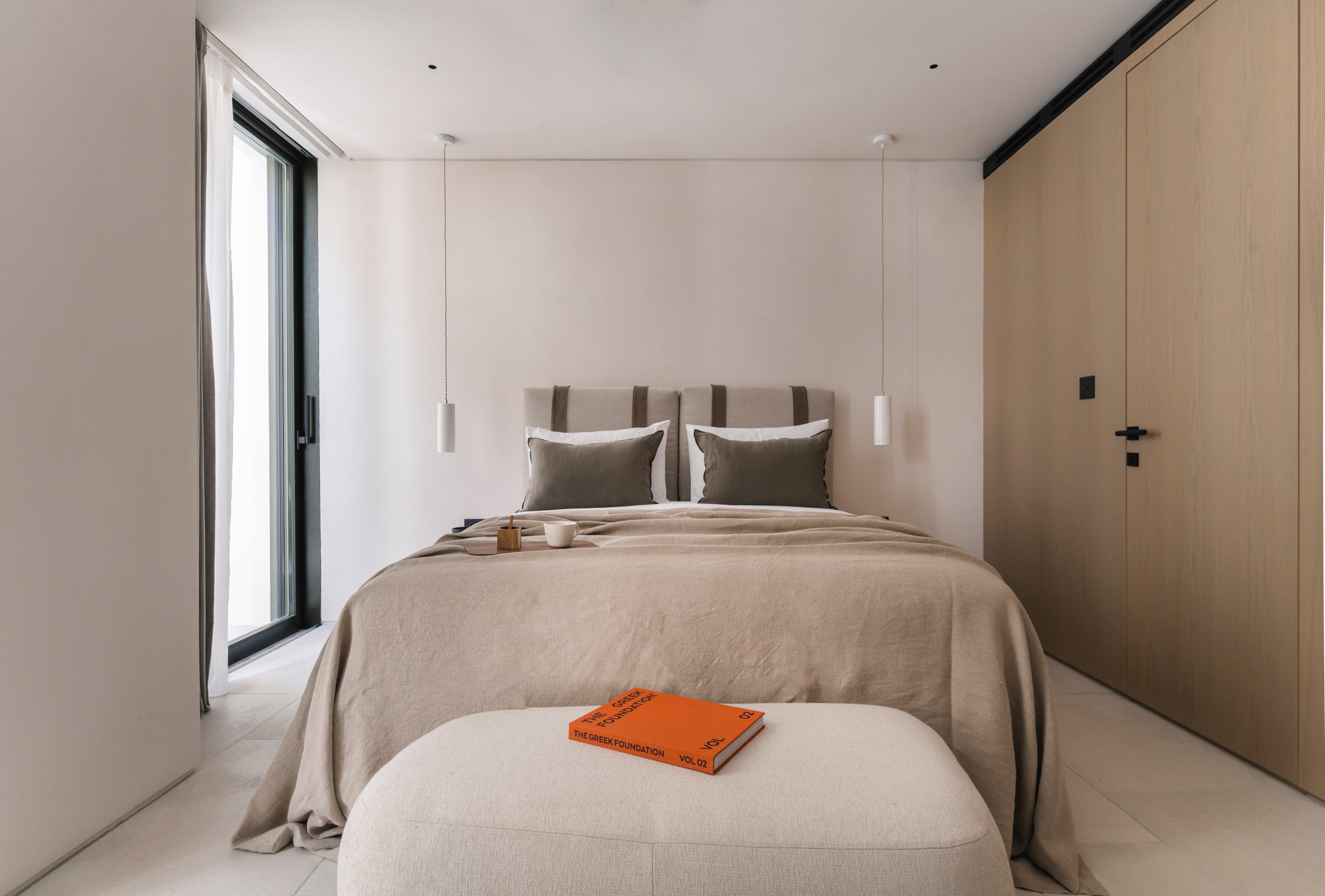 Modern bedroom with a bed, ottoman, and window.