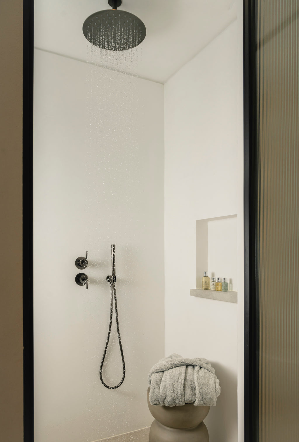 Modern shower setup with black fixtures and a towel in a bathroom.
