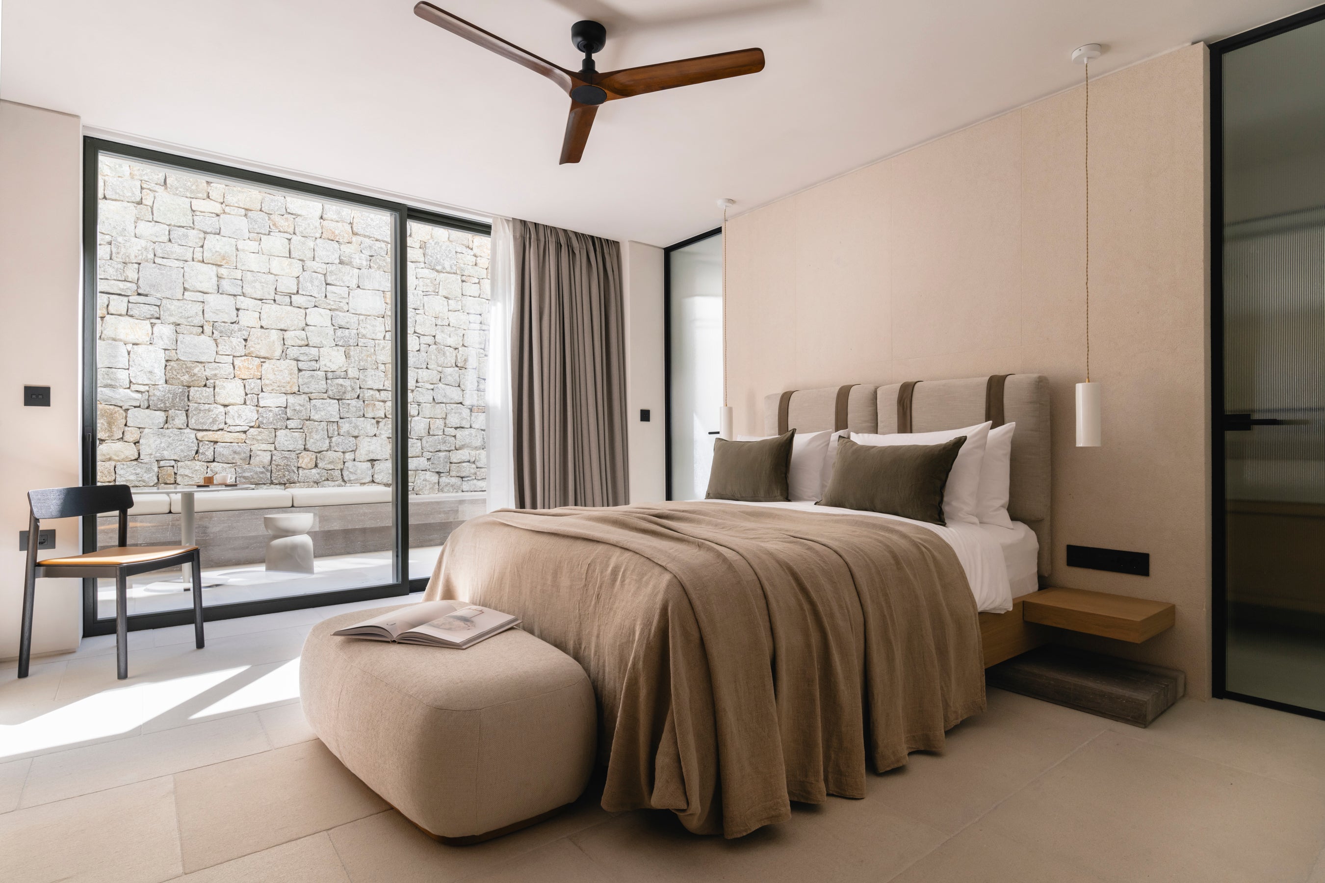 Modern bedroom with a bed, ottoman, and large windows.