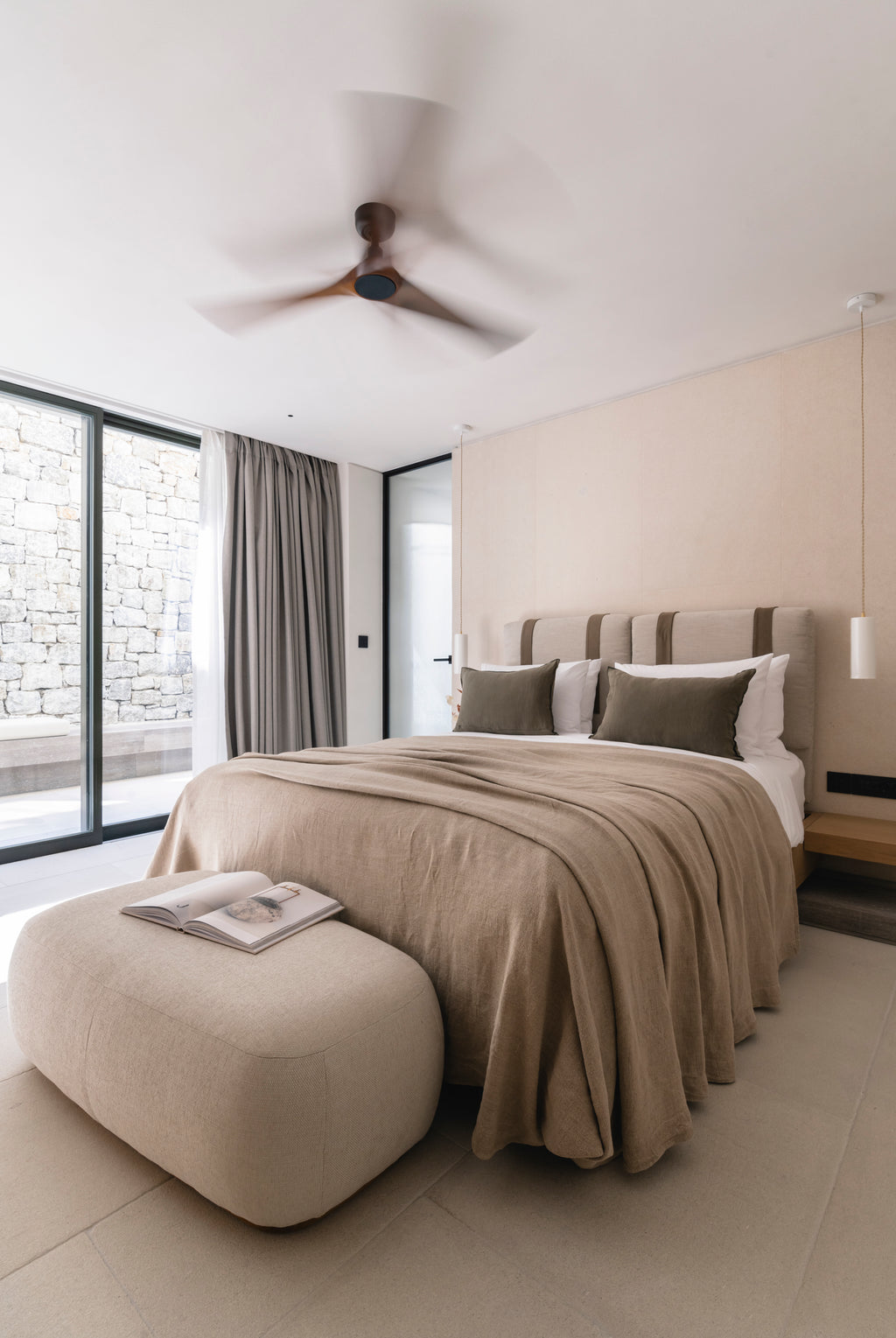 Modern bedroom with a bed, ottoman, and large windows.