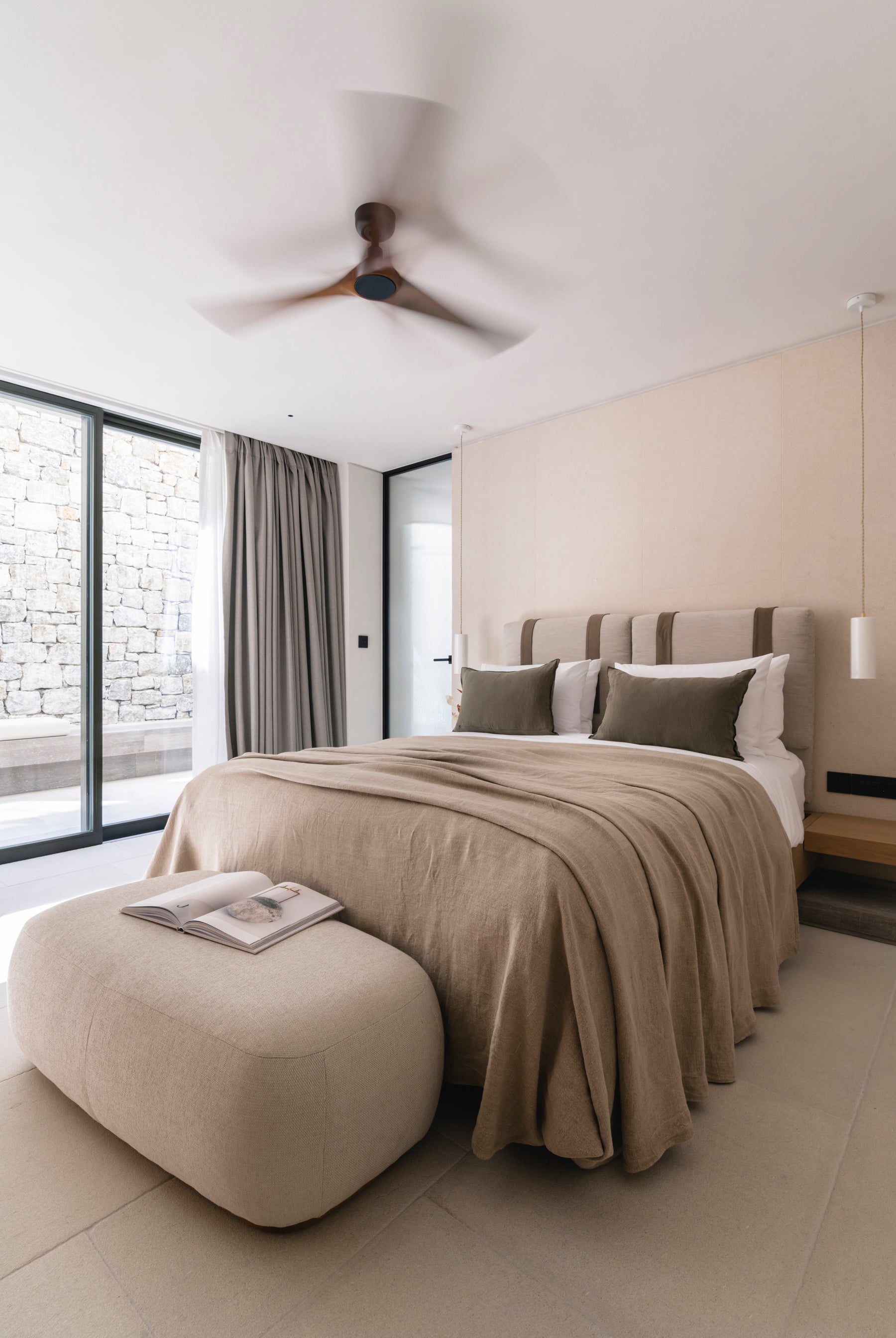 Modern bedroom with a bed, ottoman, and large windows.