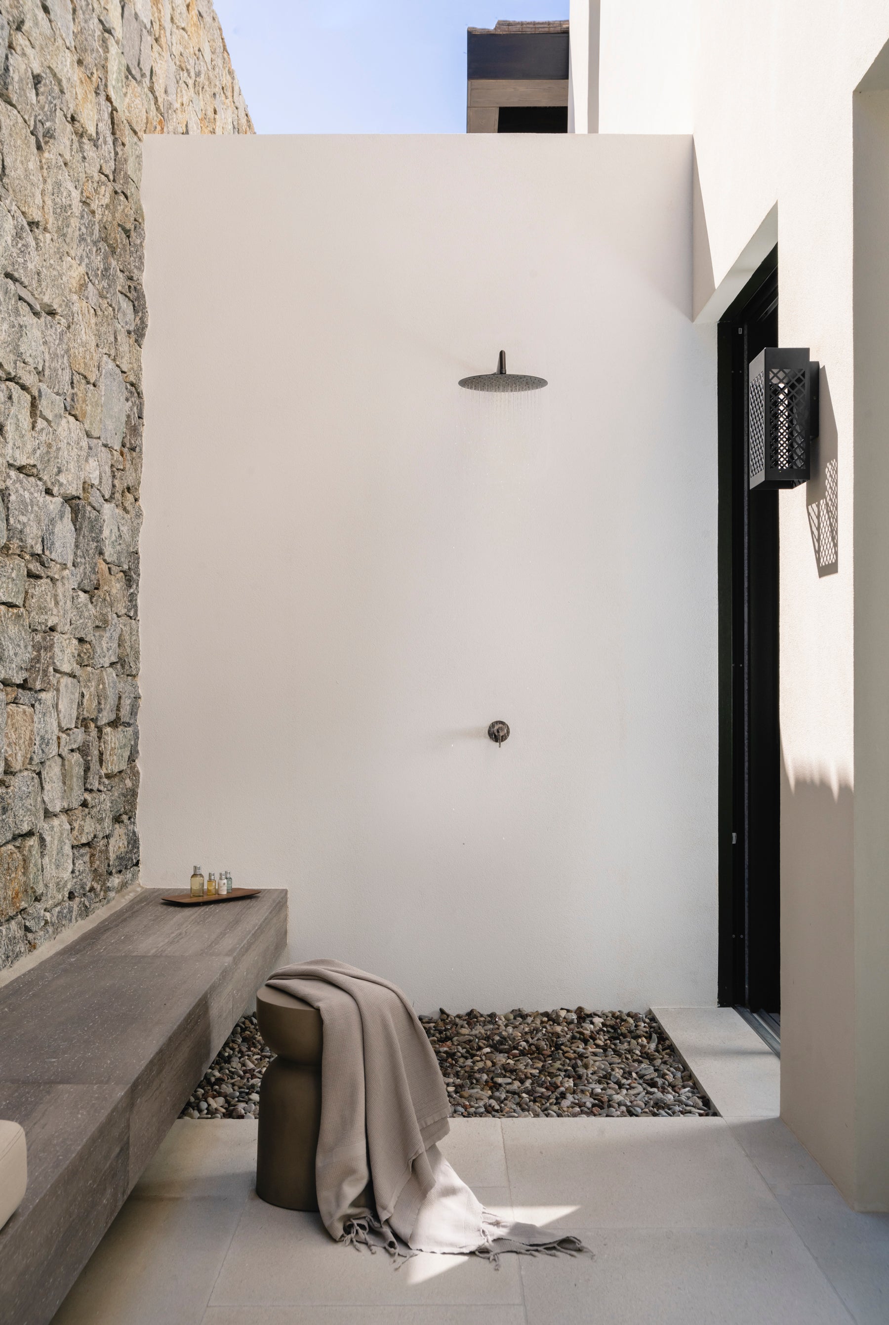 Modern outdoor shower area with stone wall and bench.