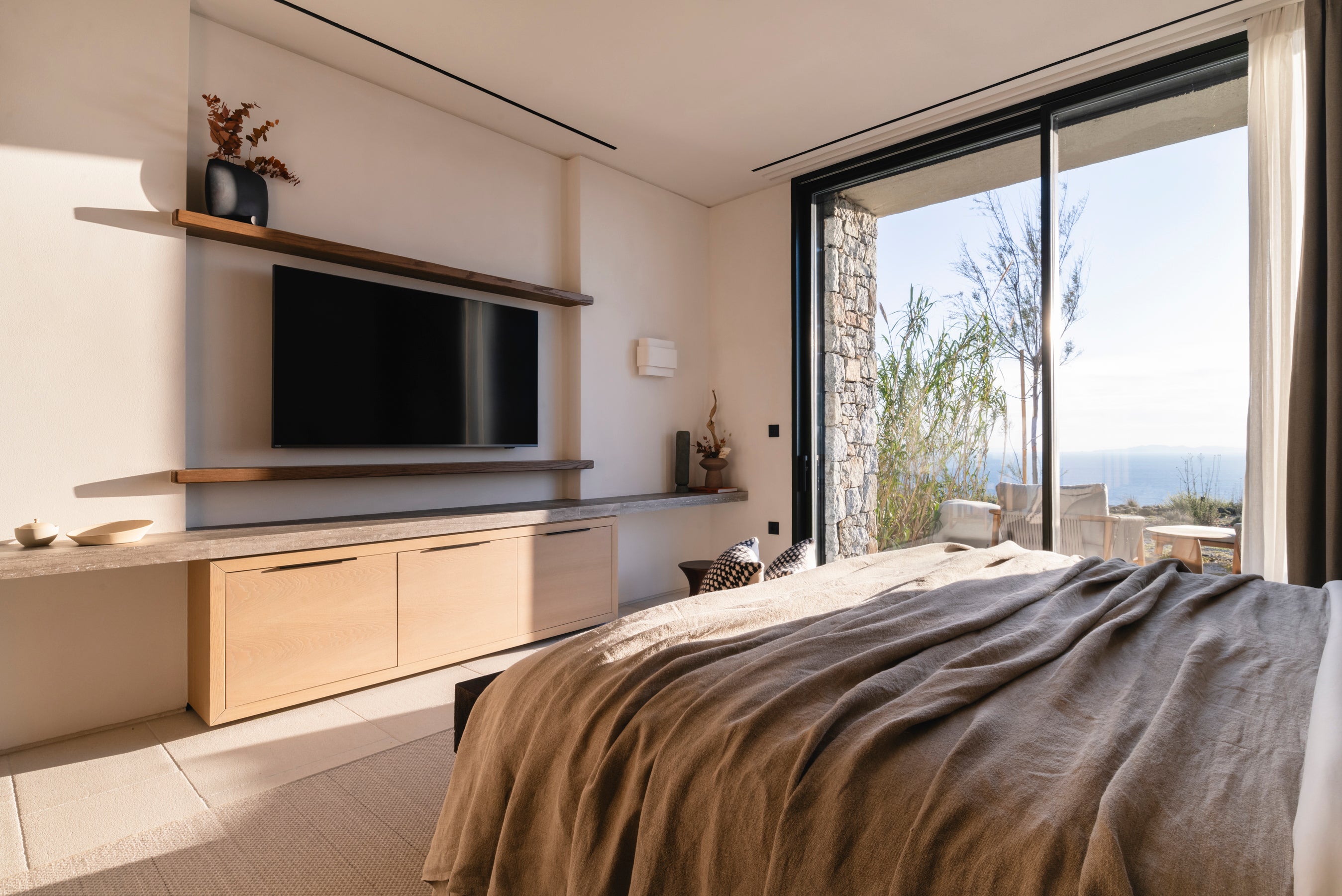 Modern bedroom with a large bed, TV, and large windows overlooking nature.