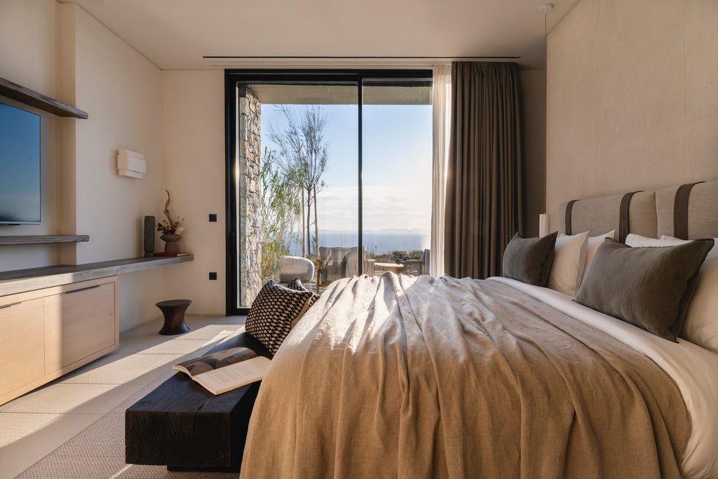 Modern bedroom with a large bed, TV, and view of trees and sky.