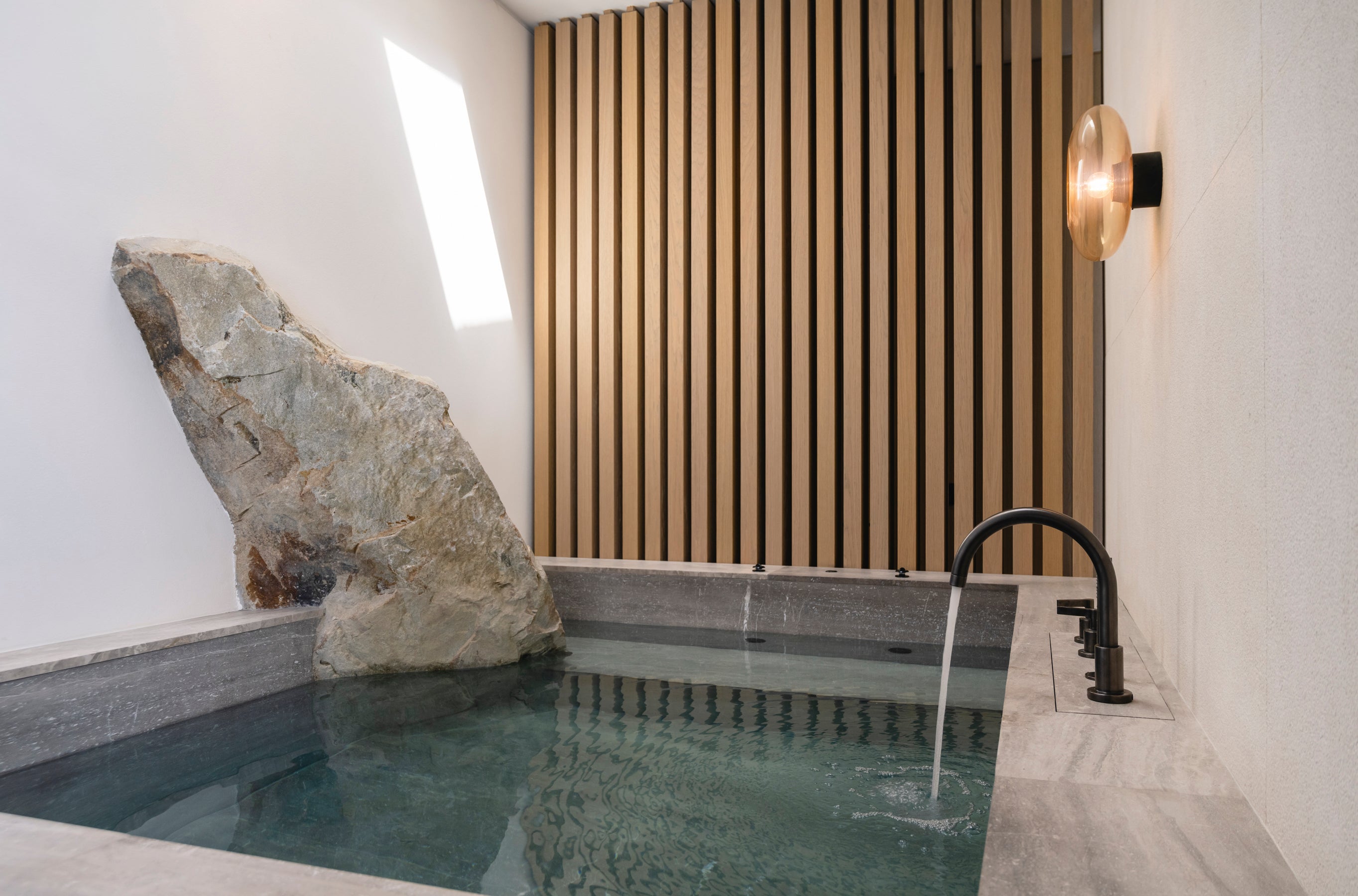 Indoor hot tub with a stone wall and wooden paneling in a modern setting