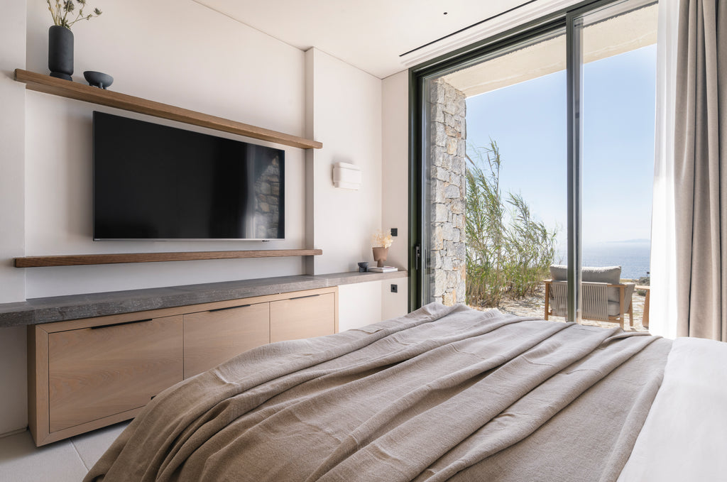 Modern bedroom with a large bed, TV, and sliding glass door leading to an outdoor area.