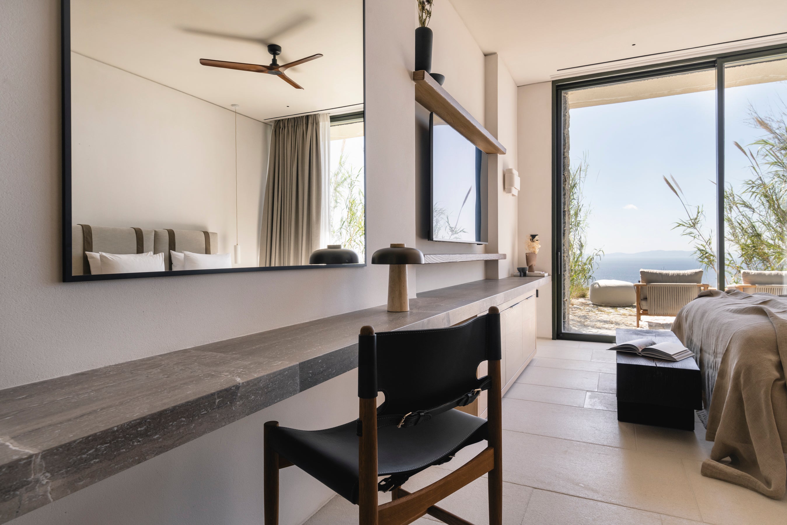 Modern bedroom with a desk, chair, and large window overlooking an ocean view.