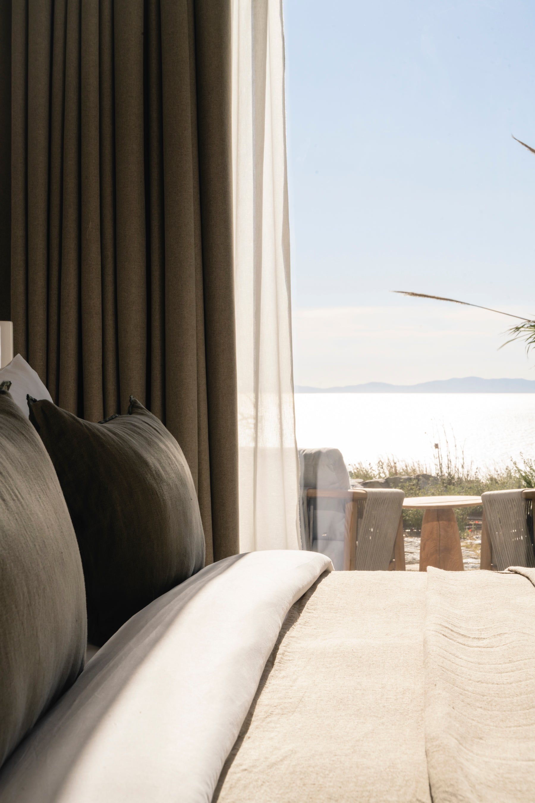 Bed with pillows and a view of a beach through curtains