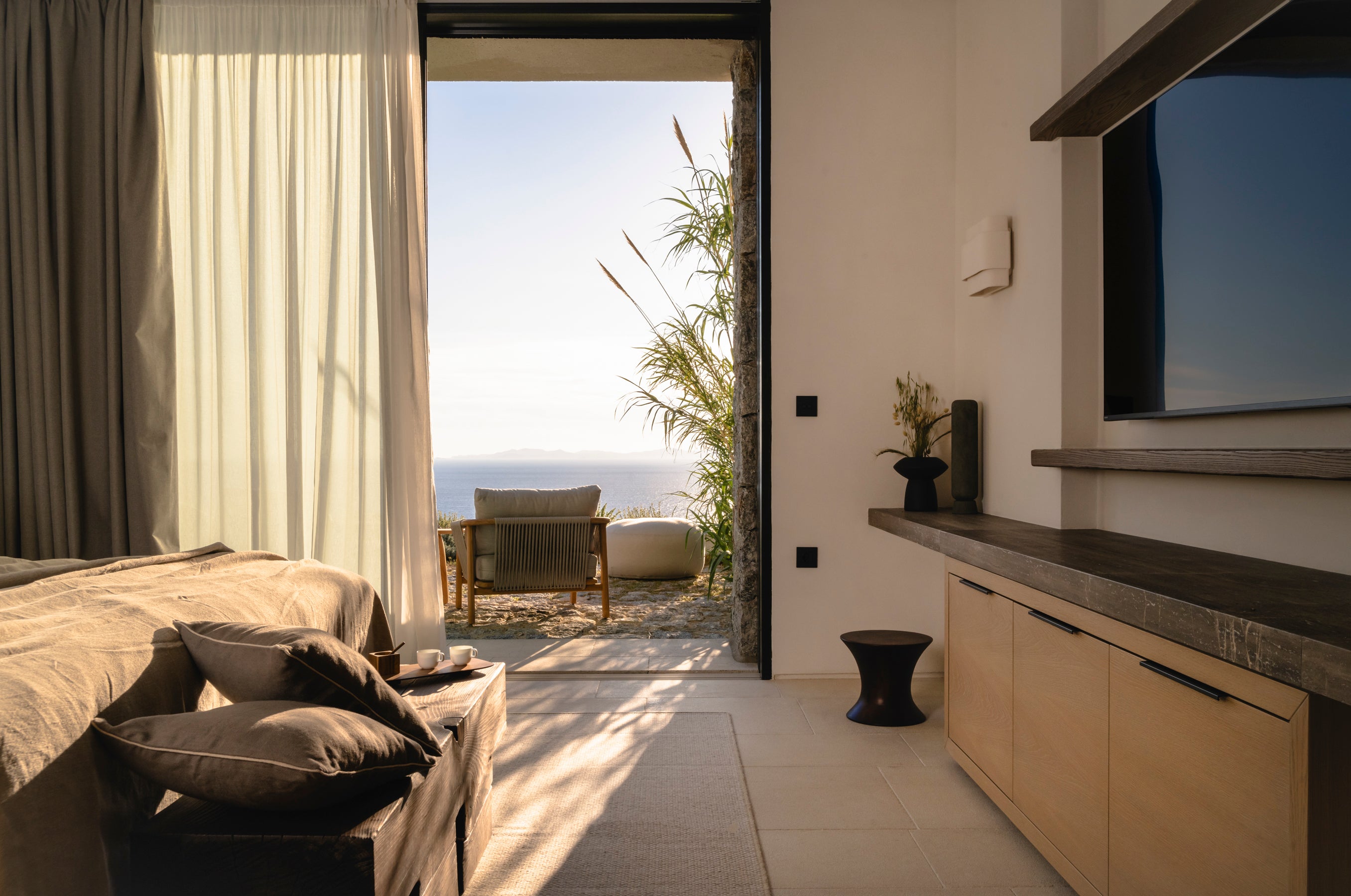 Modern bedroom with a view of the ocean through a large window.