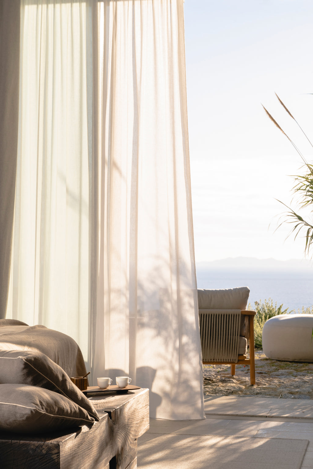 Beige outdoor sofa with cushions and a view of the ocean through sheer curtains.