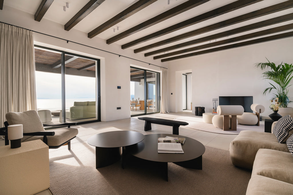 Modern living room with white walls, wooden beams, and large windows.