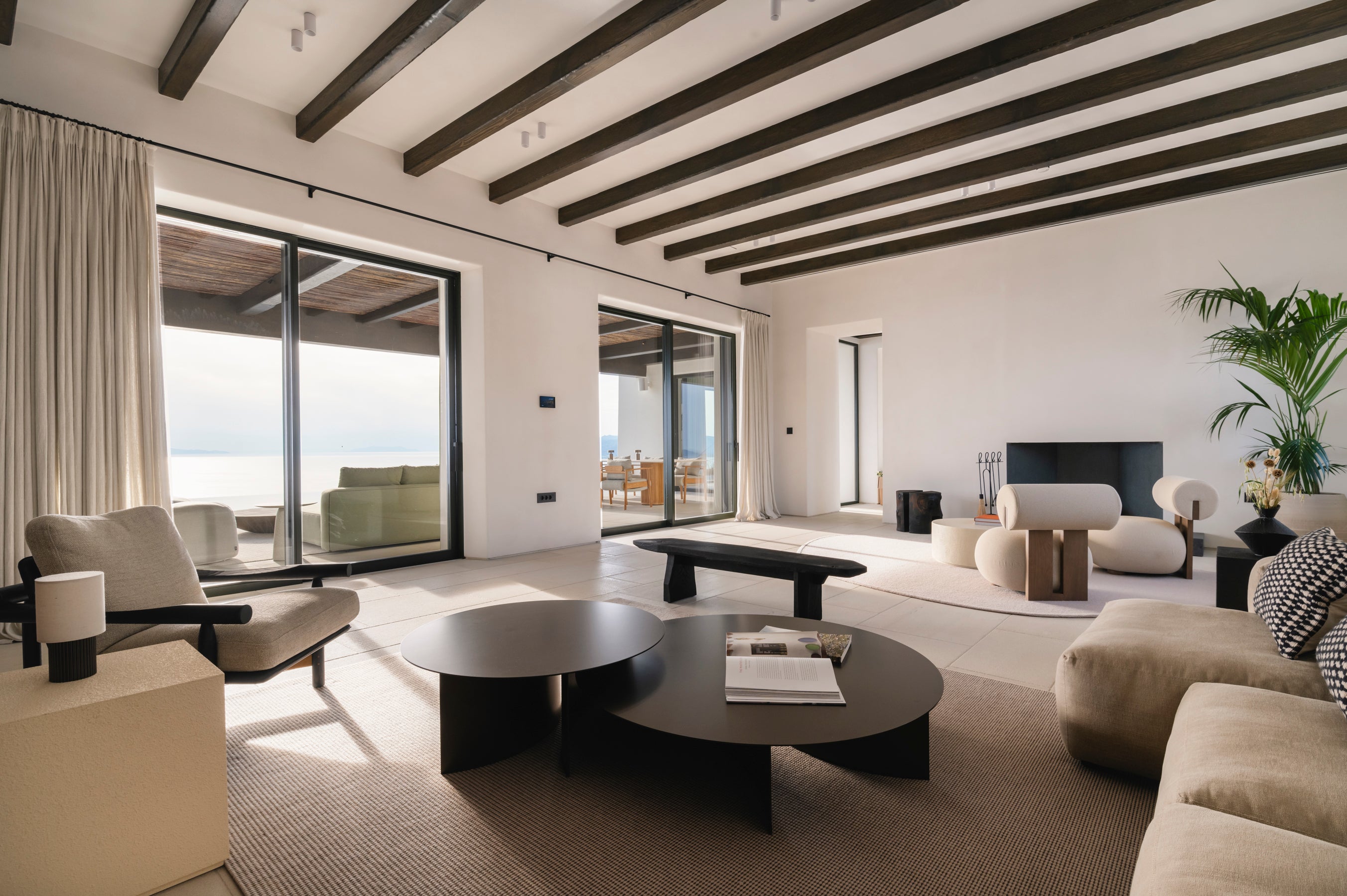 Modern living room with white walls, wooden beams, and large windows.