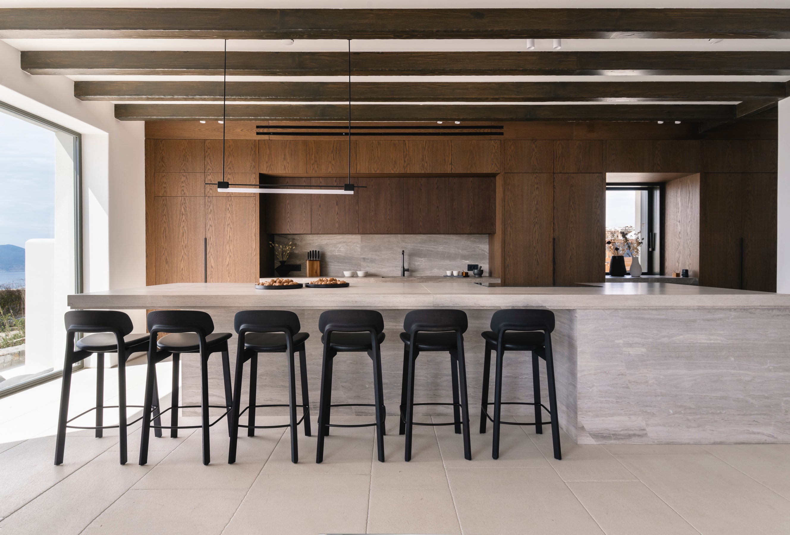 Modern kitchen with wooden cabinets, white countertops, and black bar stools.