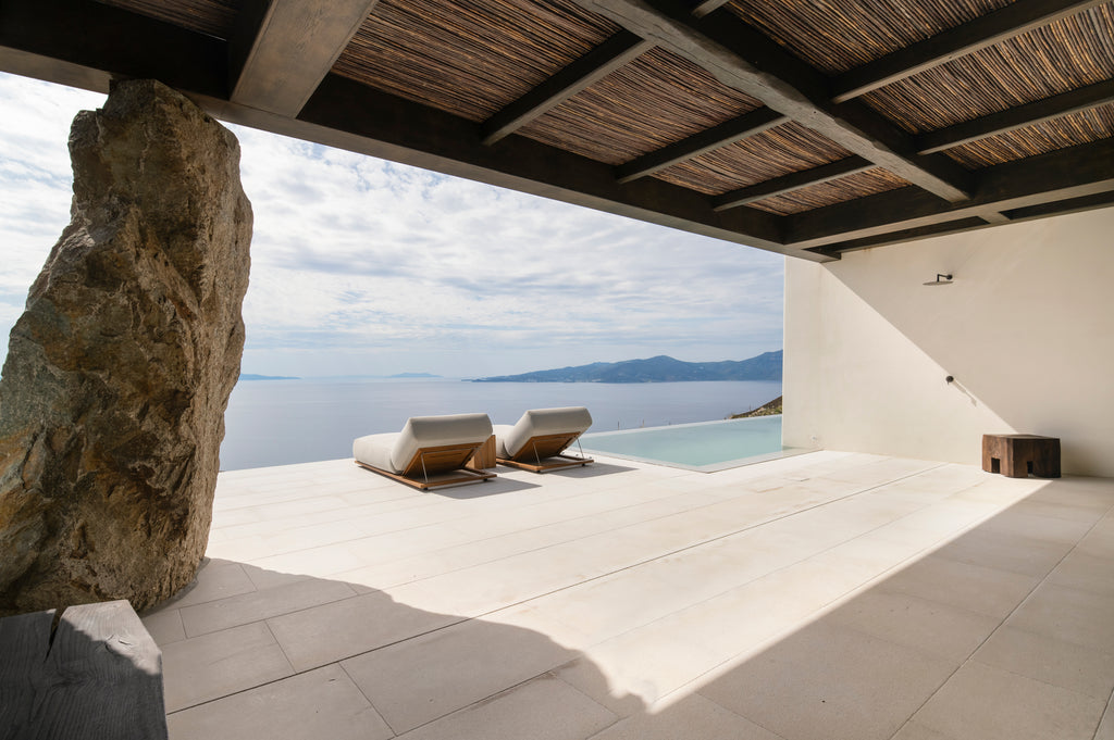 Modern outdoor patio with lounge chairs, stone wall, and pool overlooking a scenic landscape.