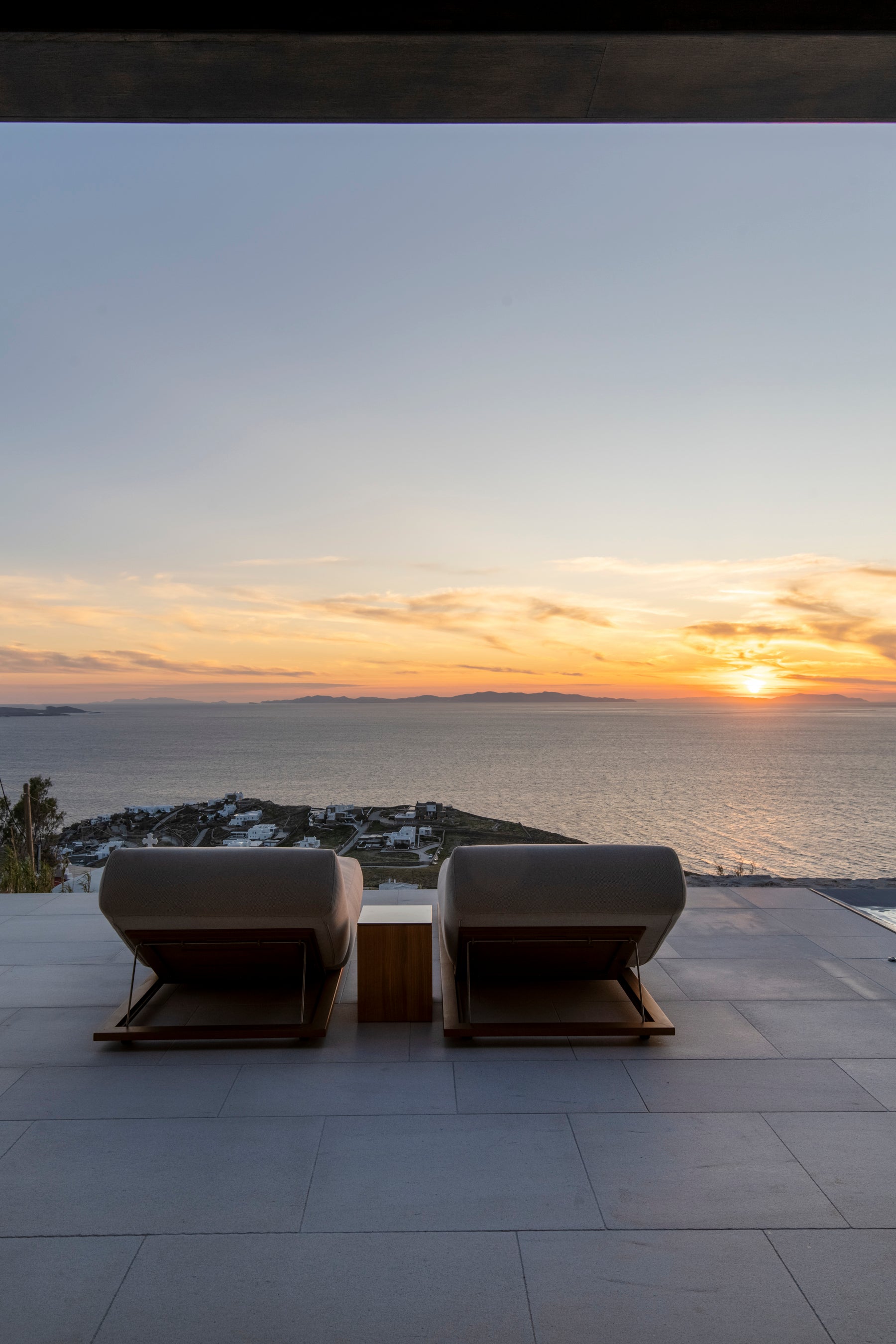 Two modern chairs on a rooftop overlooking a sunset over the ocean.
