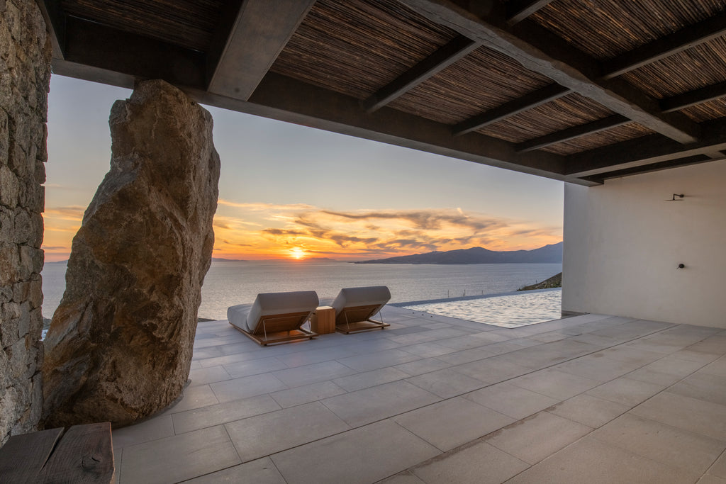 Sunset over a scenic view from a modern outdoor living space with stone walls and wooden ceiling.