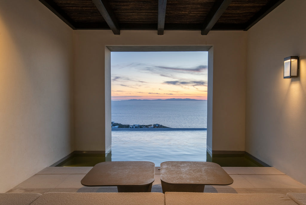 Room with a large window offering a view of the ocean at sunset.