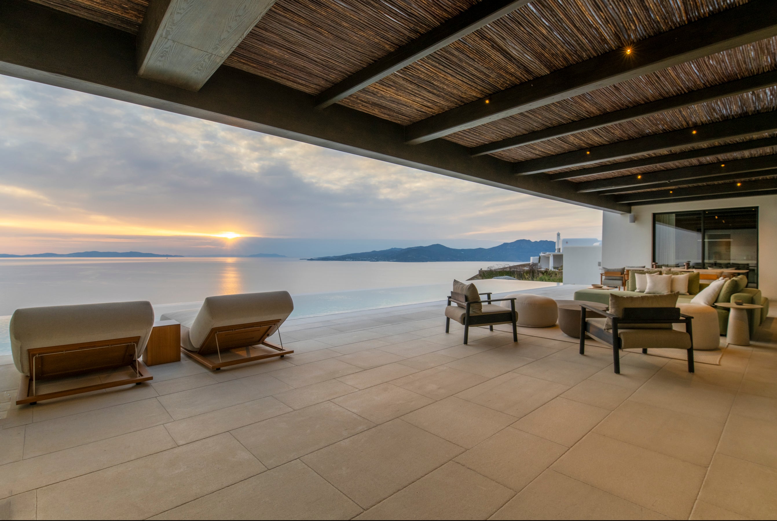 Outdoor patio area with seating and a view of the ocean during sunset.