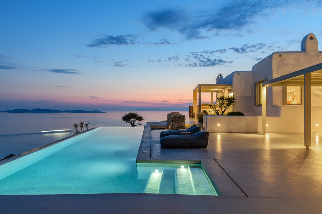 Luxury outdoor pool area with a house and ocean view at dusk.