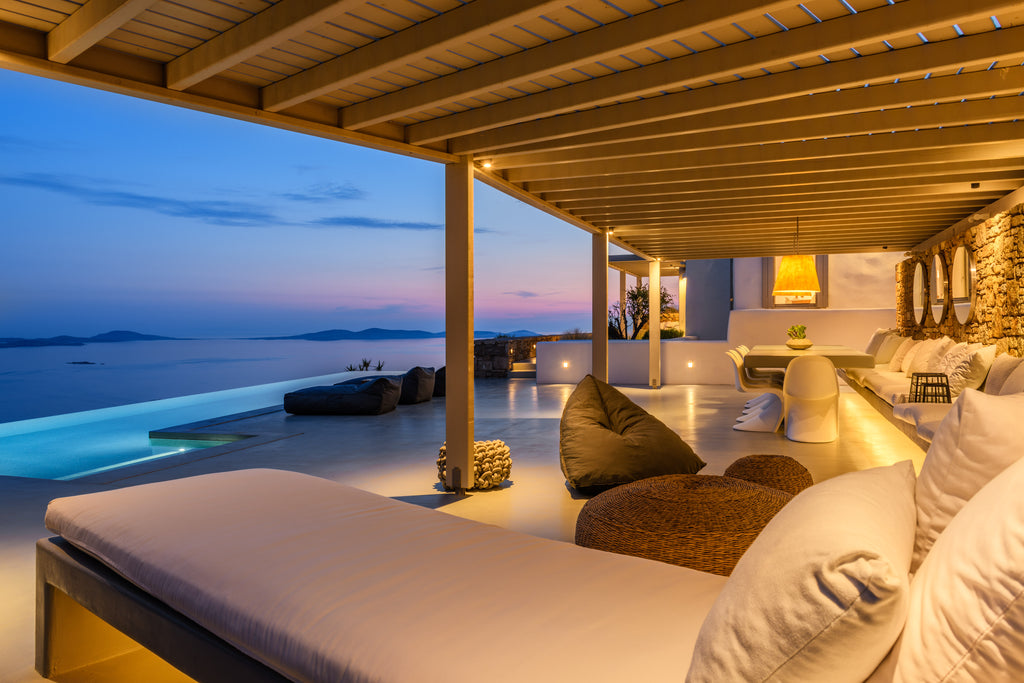 Outdoor lounge area with pool and ocean view at dusk
