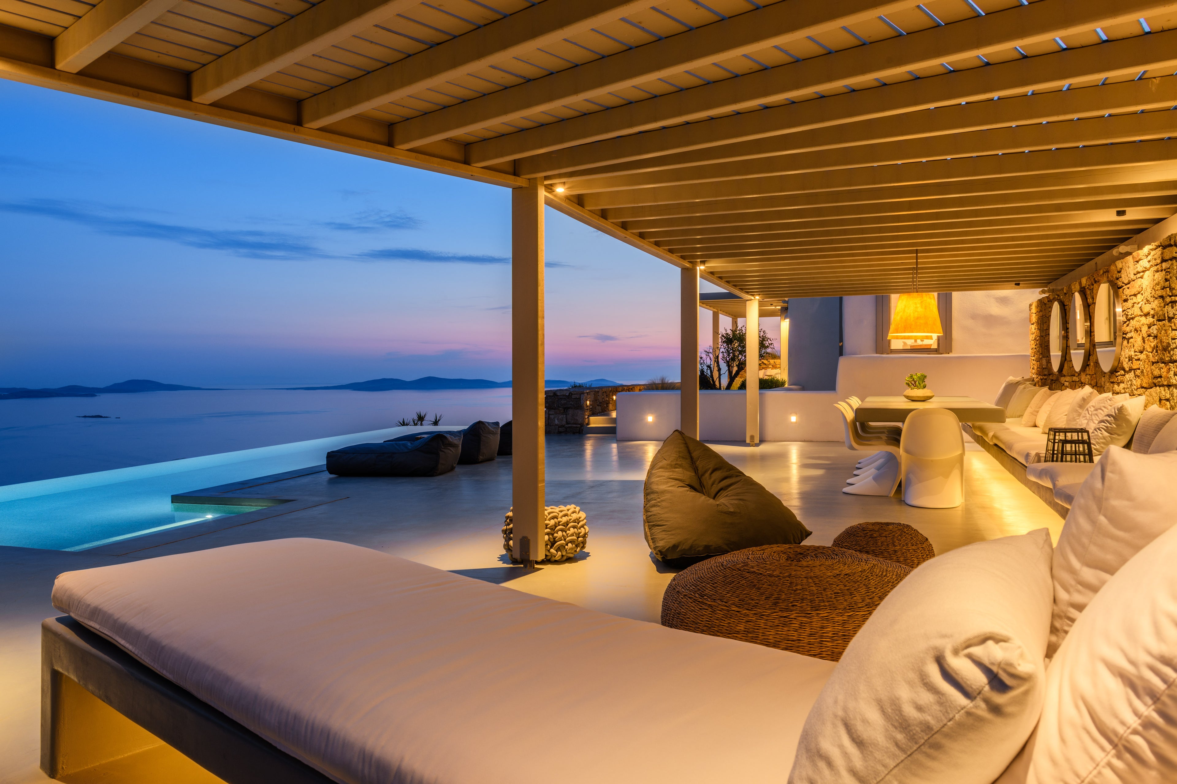Outdoor lounge area with pool and ocean view at dusk