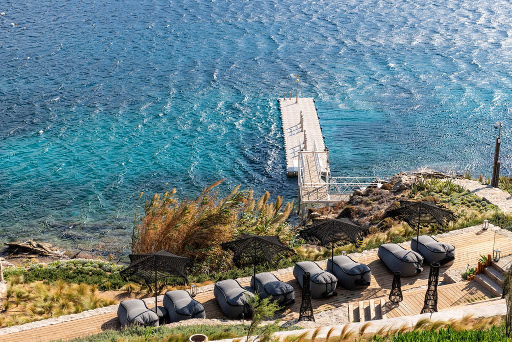 Pier extending into a body of water with umbrellas and chairs on a sunlit day.