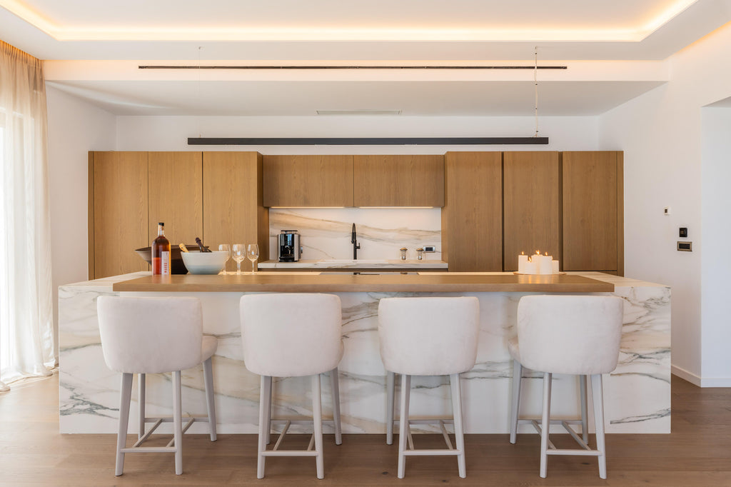 Modern kitchen with wooden cabinets, marble island, and white bar stools.