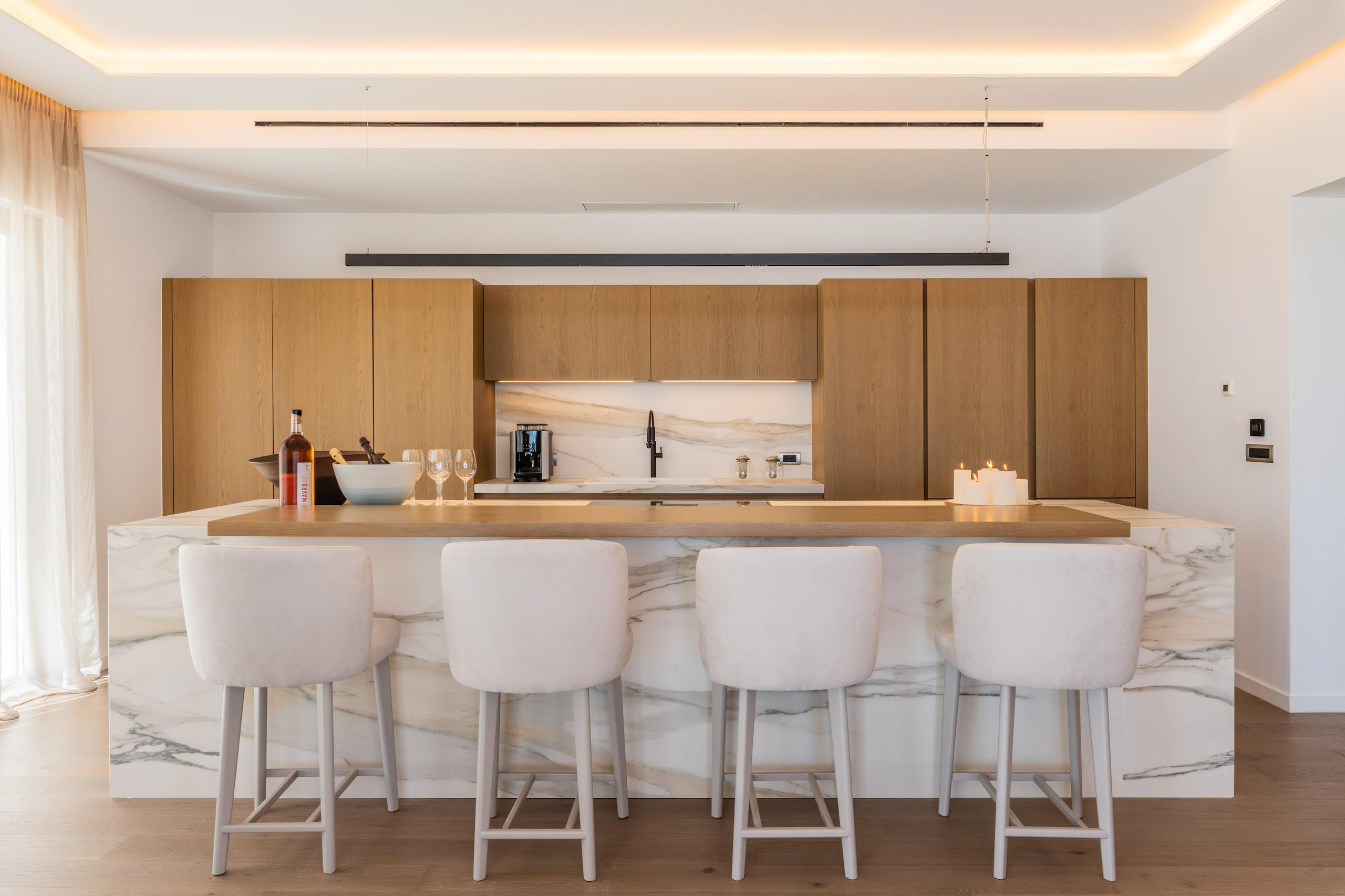 Modern kitchen with wooden cabinets, marble island, and white bar stools.